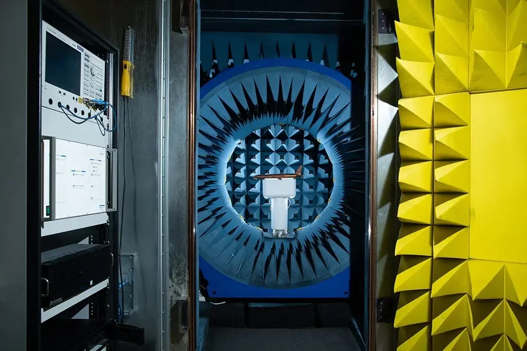 A scale model aircraft mounted on a pedestal inside UW–Madison's anechoic chamber, surrounded by blue and yellow radio-frequency absorber cones, with test instruments in the foreground.