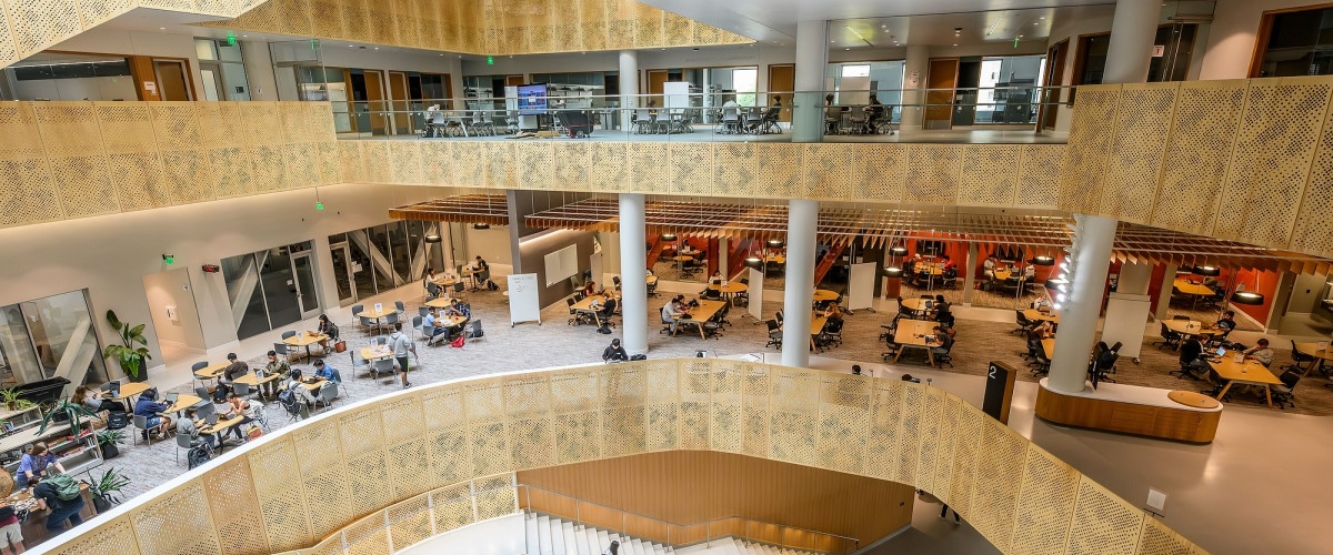 The multi-level atrium of Morgridge Hall, home of the College of Computing & Artificial Intelligence, with students studying at tables across open floors.